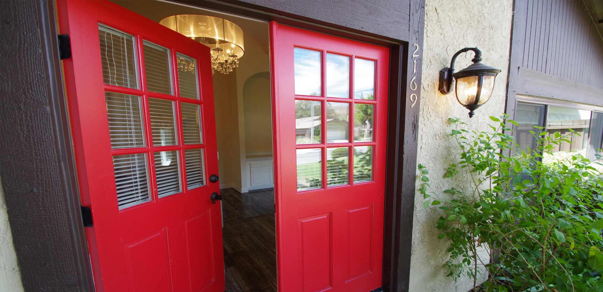A pair of red French doors opening into a home with dark wood floors and an entryway chandelier